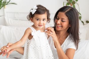 A mother and child share joyful moments together while playing and cuddling on a white bed.