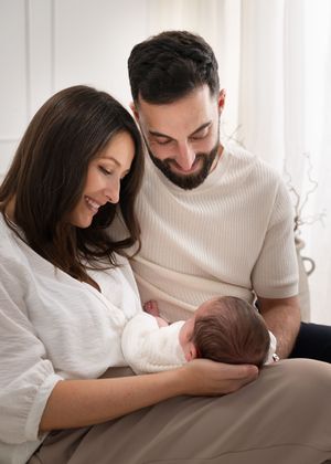 Happy parents smiling at their newborn baby, with mother cradling infant in a bright, softly lit room.