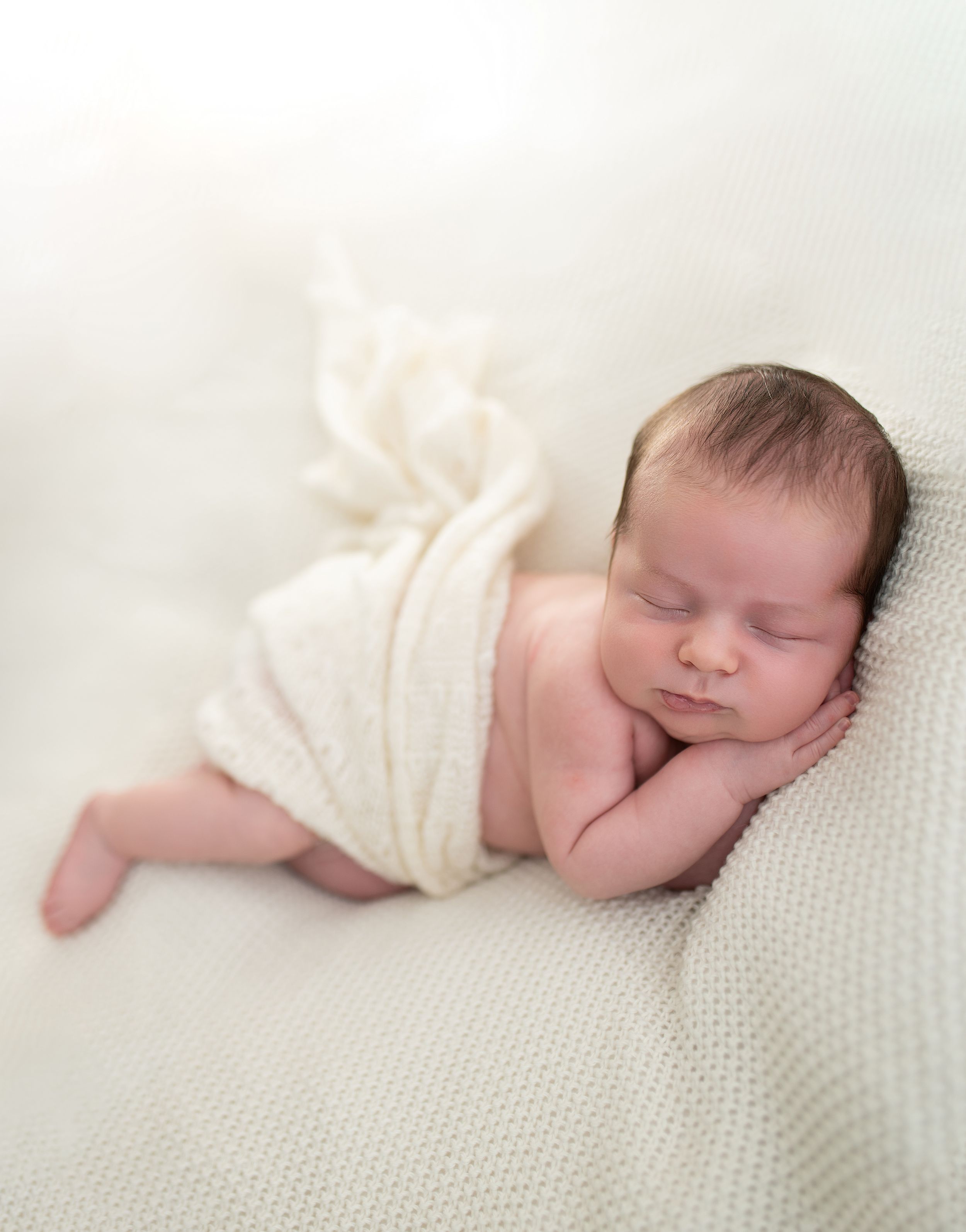 Peaceful newborn baby sleeping wrapped in a soft cream knit blanket during a professional newborn photography session.