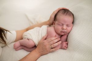 Newborn baby sleeping peacefully wrapped in white blanket while mother gently holds and cradles the infant.