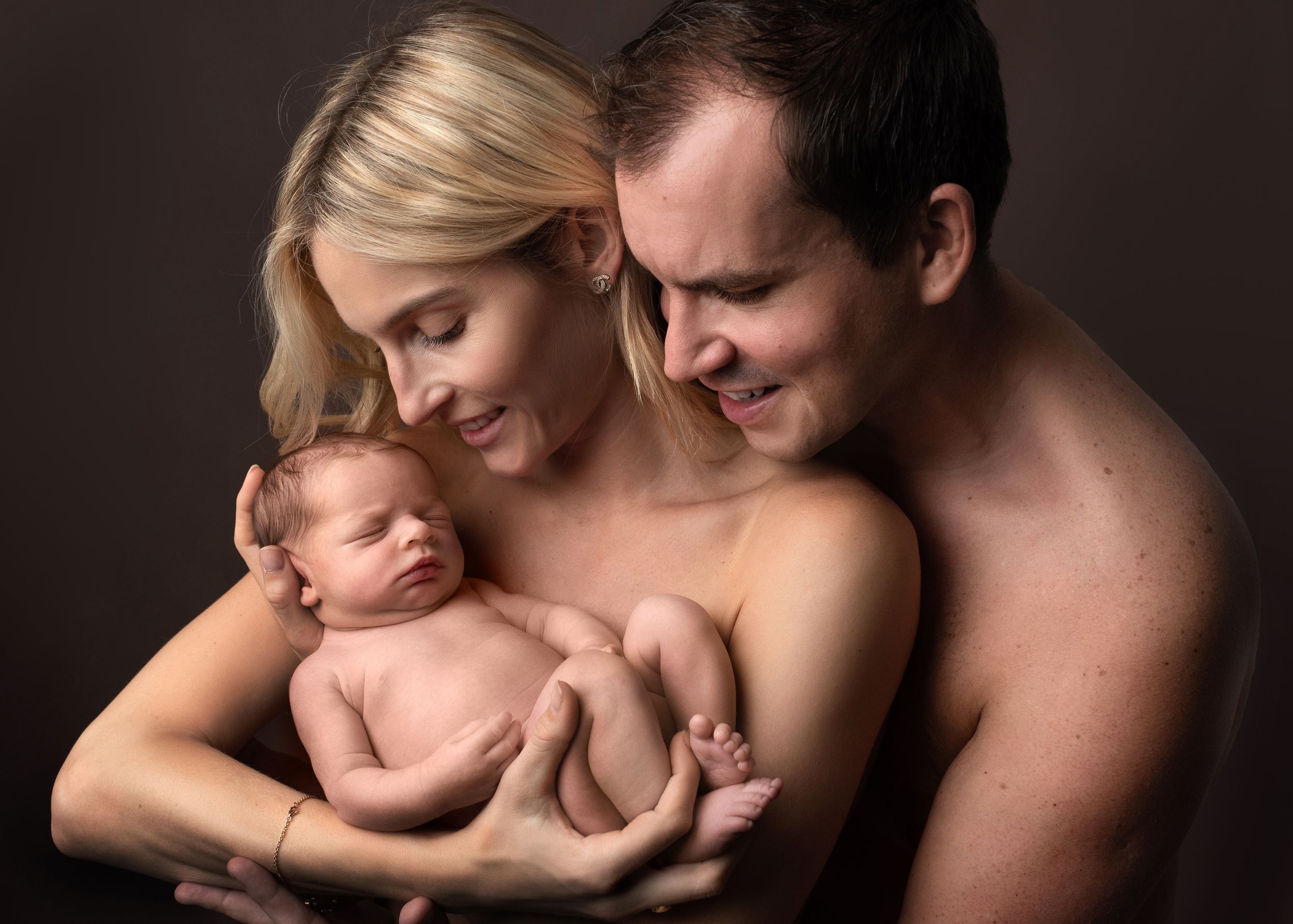 Intimate black and white portrait series showing tender moments between a couple with their newborn baby.