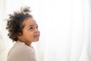 A curly-haired child looks upward with a bright smile against a light background.