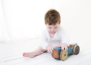A series of four images showing a baby lying on white sheets playing with a vintage wooden spool.