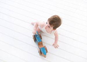 A baby in brown pants crawls across a white wooden floor while holding a blue toy block.