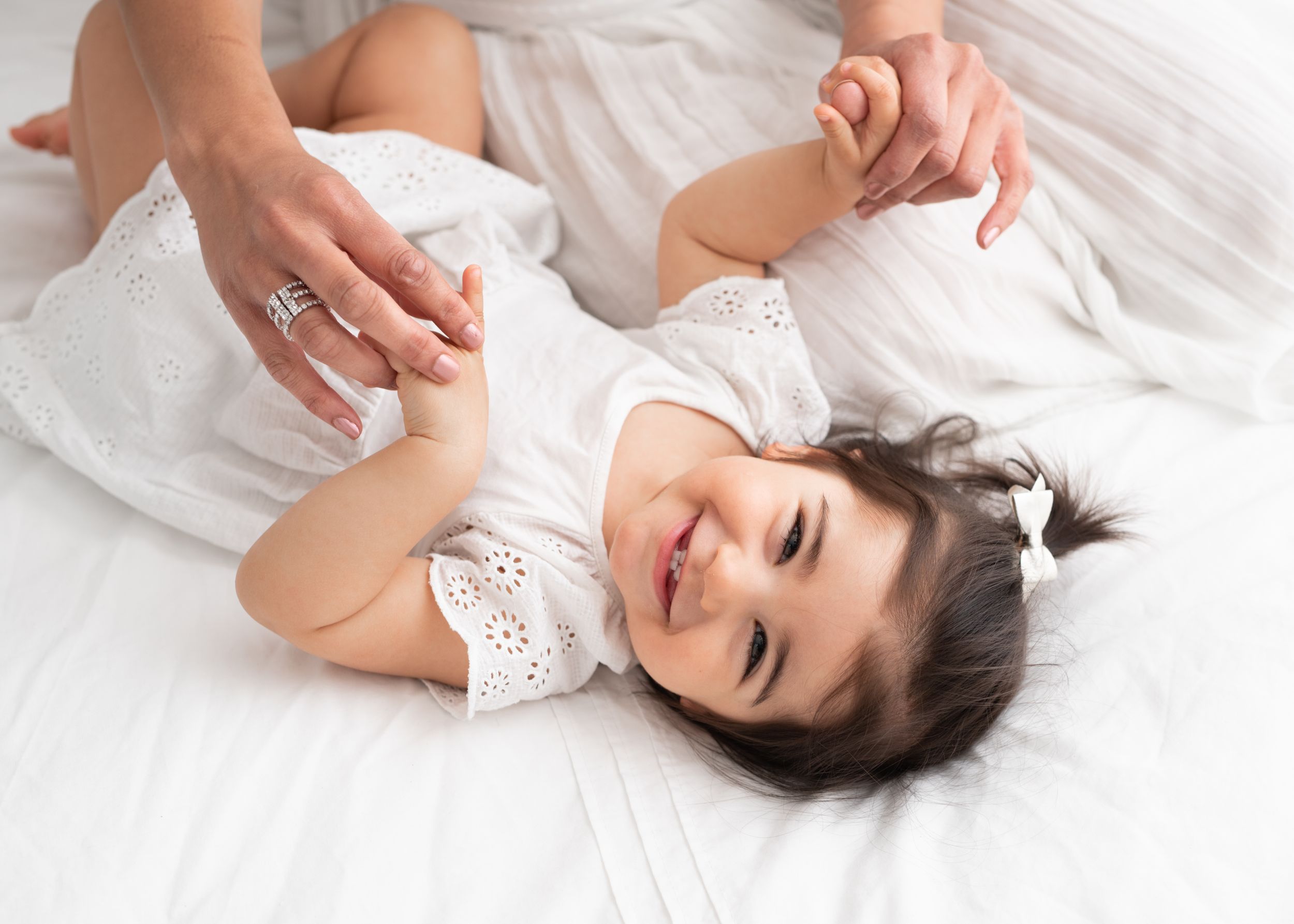Person in white clothing lying on white bedding with hands raised in relaxed poses.