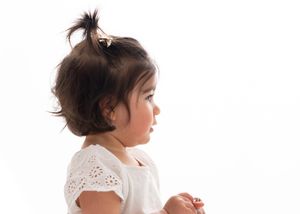A toddler in a white dress stands against a white background in a series of three poses showing different angles.