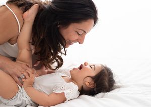 A mother and baby share an intimate bonding moment while lying together on white bedding.