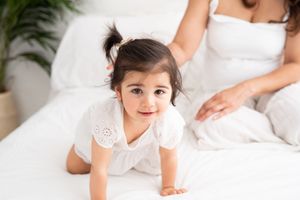 A series of connected photos showing a baby lying on white bedding and reaching out to touch someone's hand.