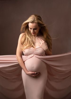 A series of artistic maternity photos showing a woman in a pink dress with flowing fabric against a dark background.
