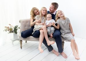 A family wearing casual clothing sits together on a white floor in a bright, airy space.
