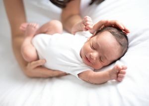 A sleeping baby wearing white clothing rests peacefully on white bedding.