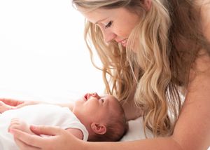 Mother and baby share tender bonding moment while lying together on white bedding.
