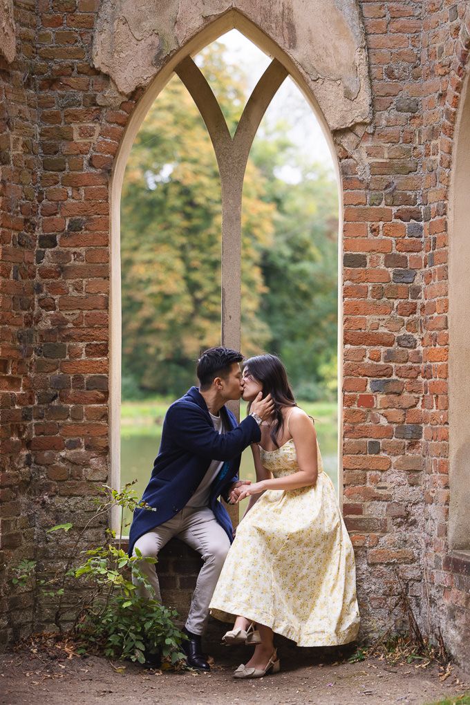 An engagement shoot of a romantic moment captured through brick archways in a garden setting with autumn trees. Painshill Park, Surrey.