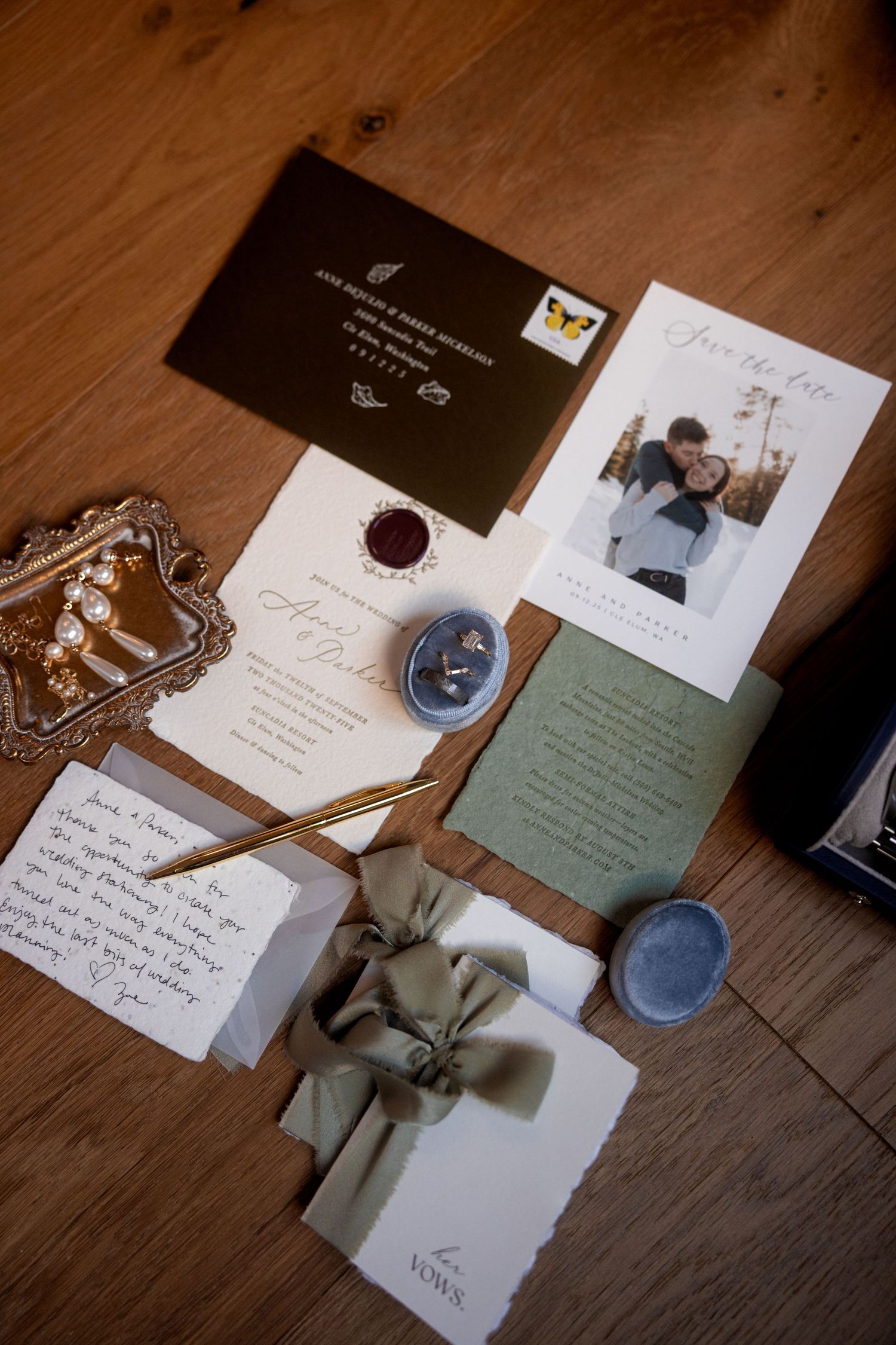 Wedding invitation suite with wax seal, handwritten notes, and photographs laid out on wooden floor.