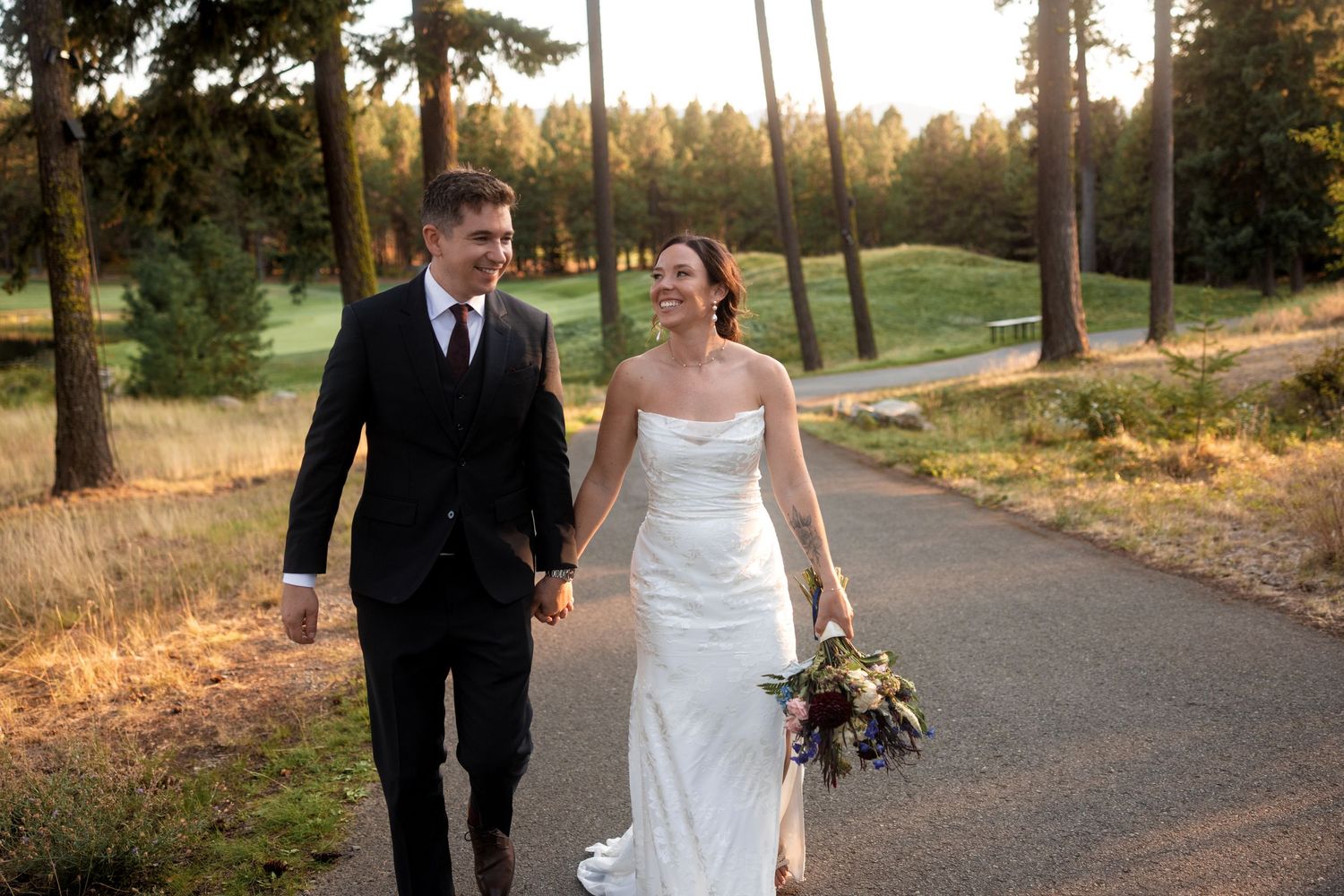Newlyweds walking together on a tree-lined path at sunset.