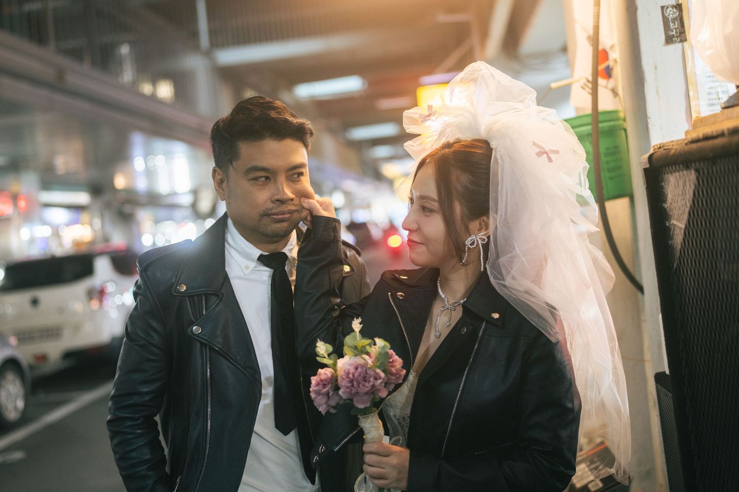 A couple in formal attire shares a romantic moment in what appears to be a parking garage setting.