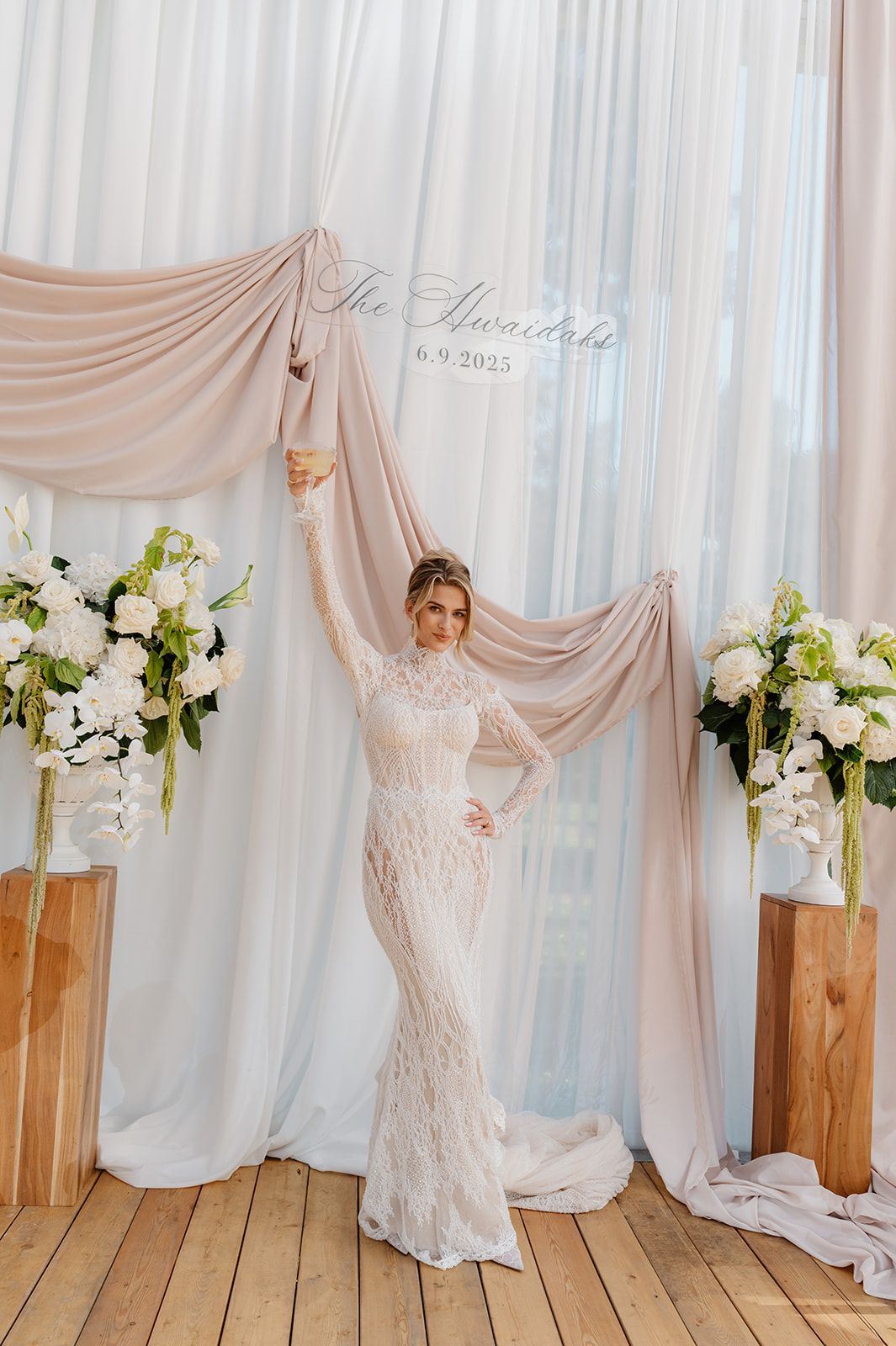 Wedding dress display against white draped backdrop with wooden pedestals and floral arrangements.