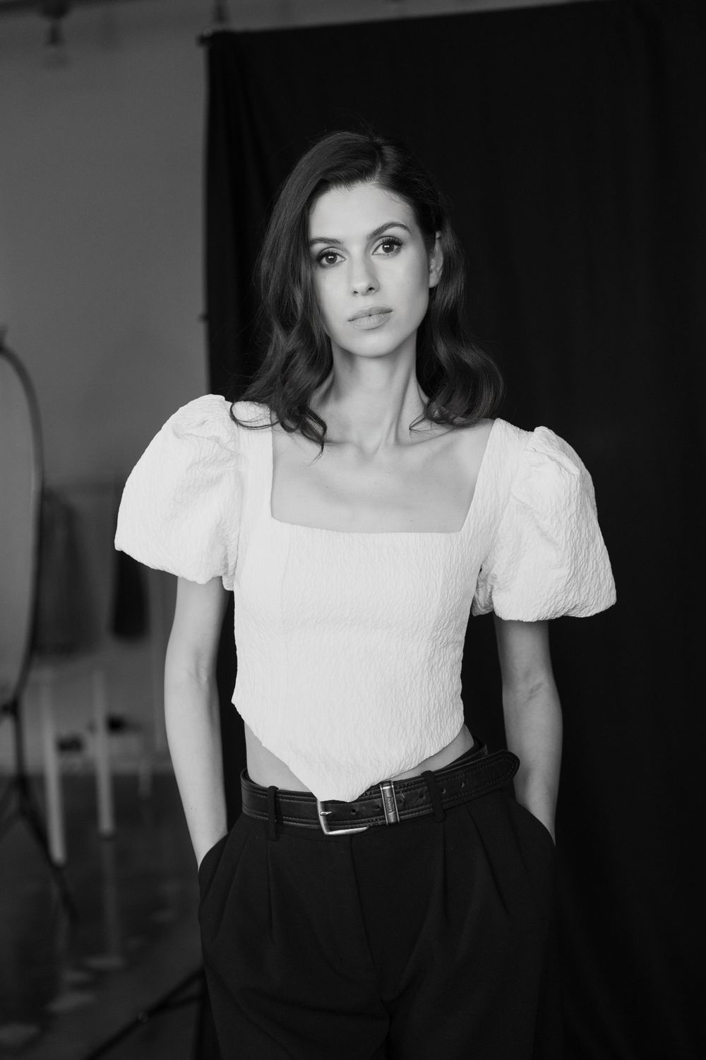 Black and white portrait series showing figure in white blouse and dark high-waisted pants against dark background.