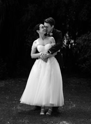 A romantic black and white wedding photo showing a couple embracing in a tea-length dress and suit outdoors.