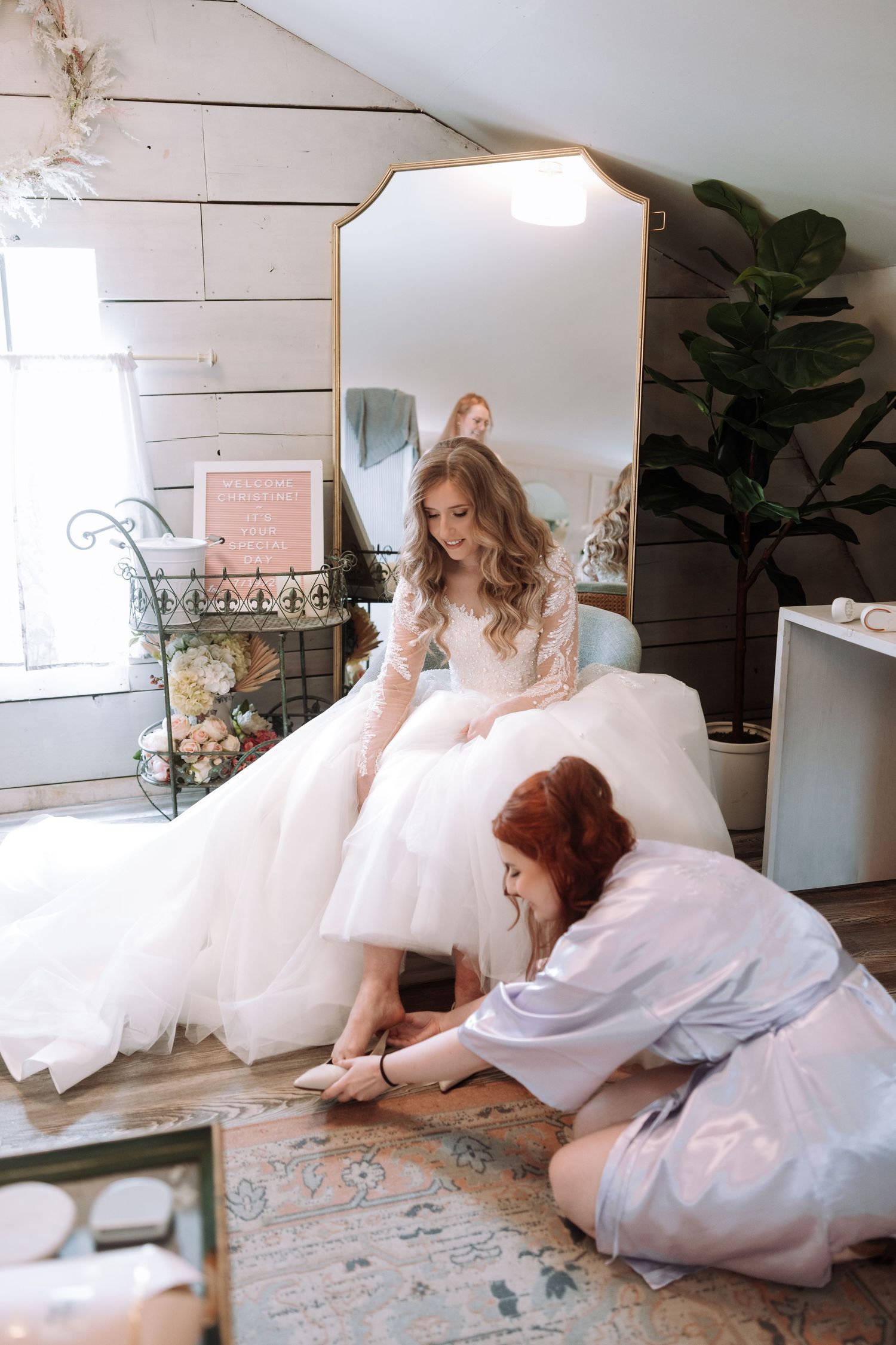 Flowing white wedding dress spread across a rustic wooden floor in natural light.