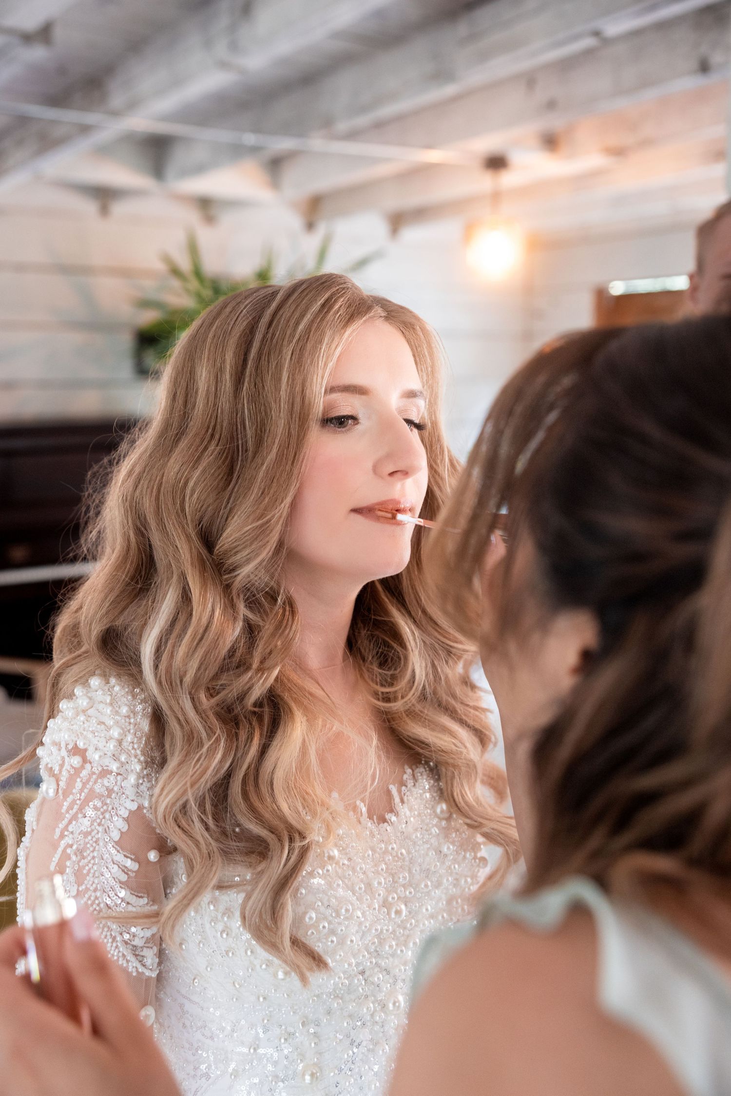 Wedding preparation scene with bride getting final touches on hair and makeup.
