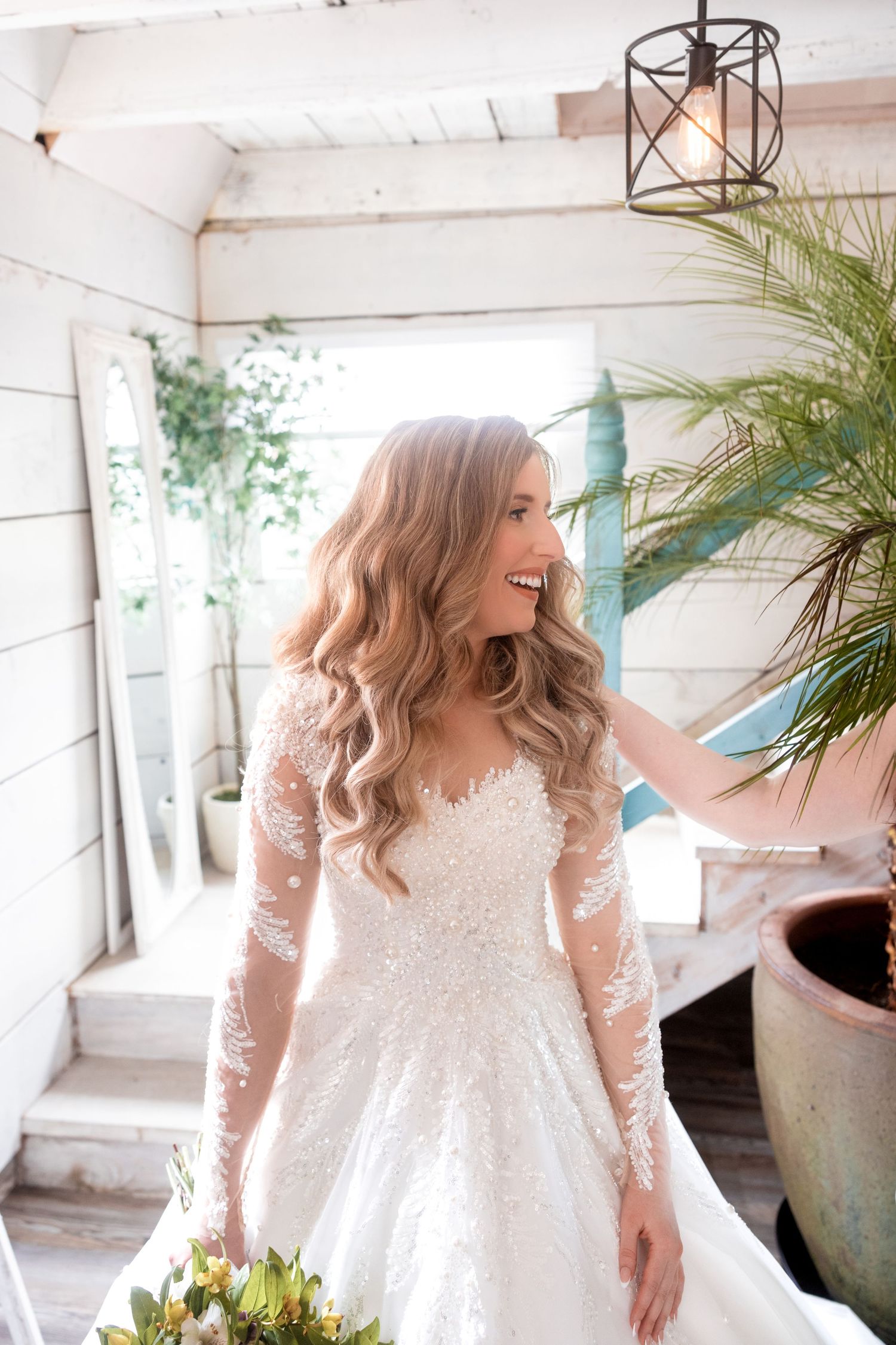 A beautiful white lace wedding gown with long sleeves photographed in a bright sunlit venue.