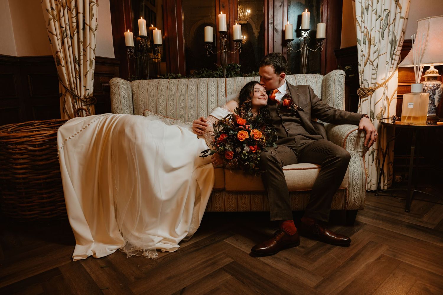 A romantic wedding scene with a couple sitting together in a cozy, dimly lit rustic room with elegant decor at bagden hall, by Daniel Berry
