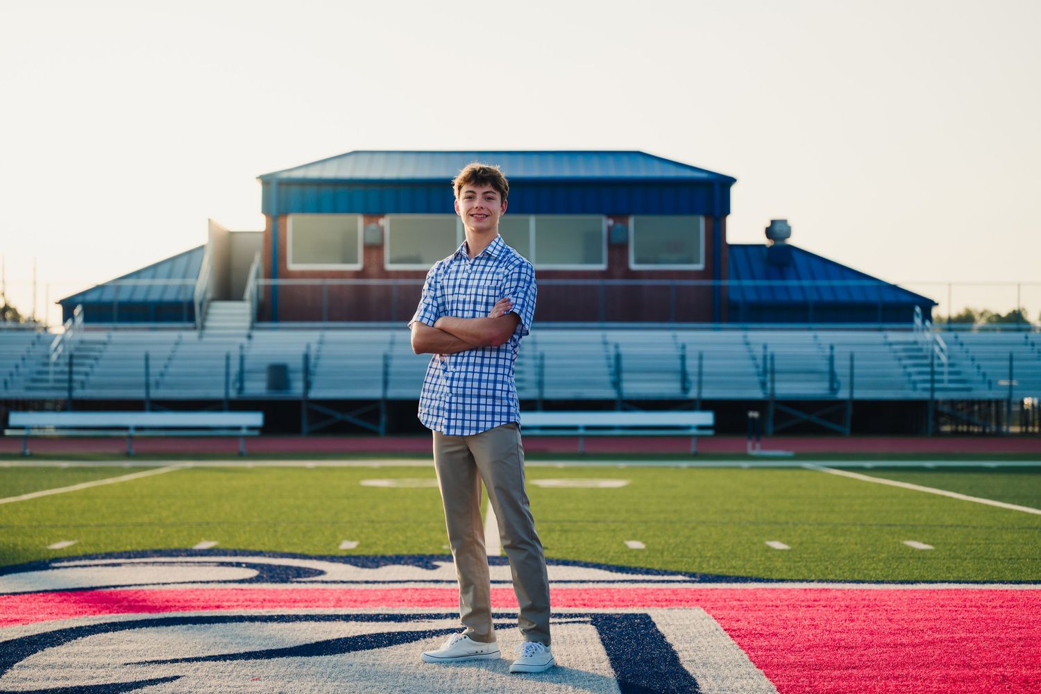 A person stands on a football field logo in front of stadium bleachers during golden hour.