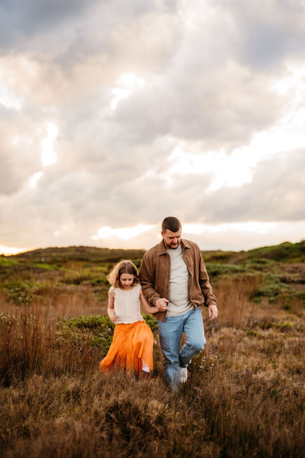 A parent and child share playful moments together in a scenic field during golden hour sunset.