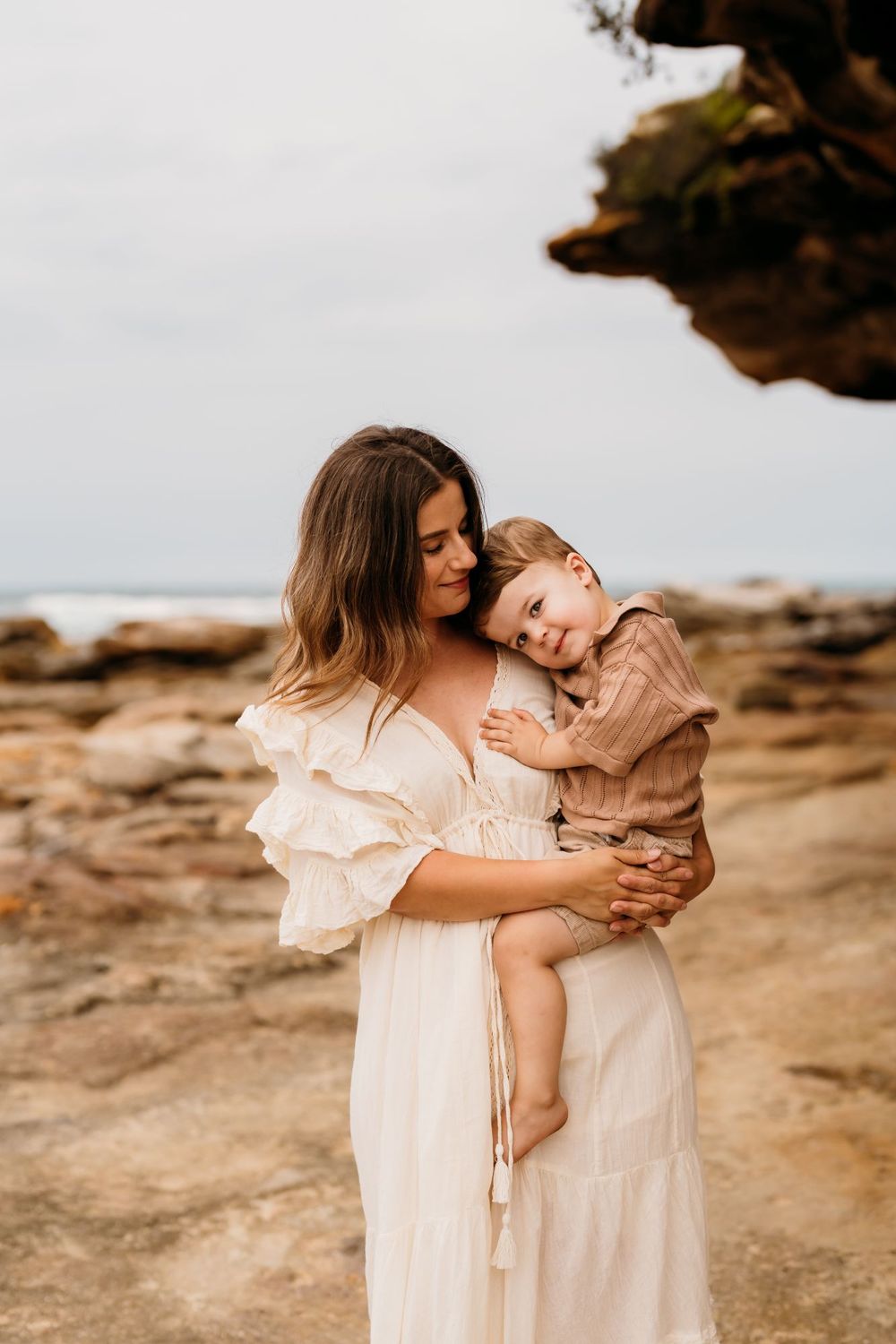 A mother and child cuddle amongst sandstone rocks on Sydney beach