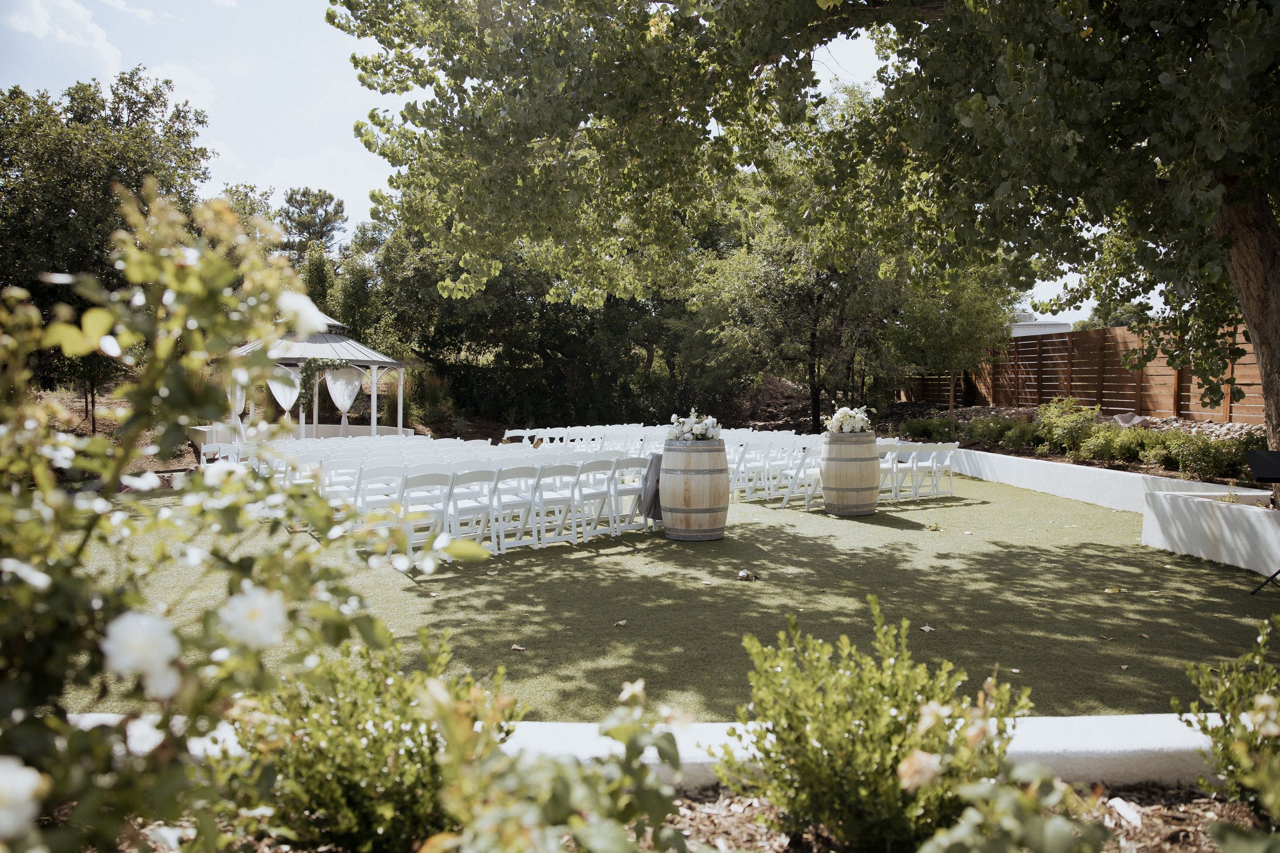 White folding chairs arranged in rows for an outdoor garden wedding ceremony under sunlit trees.