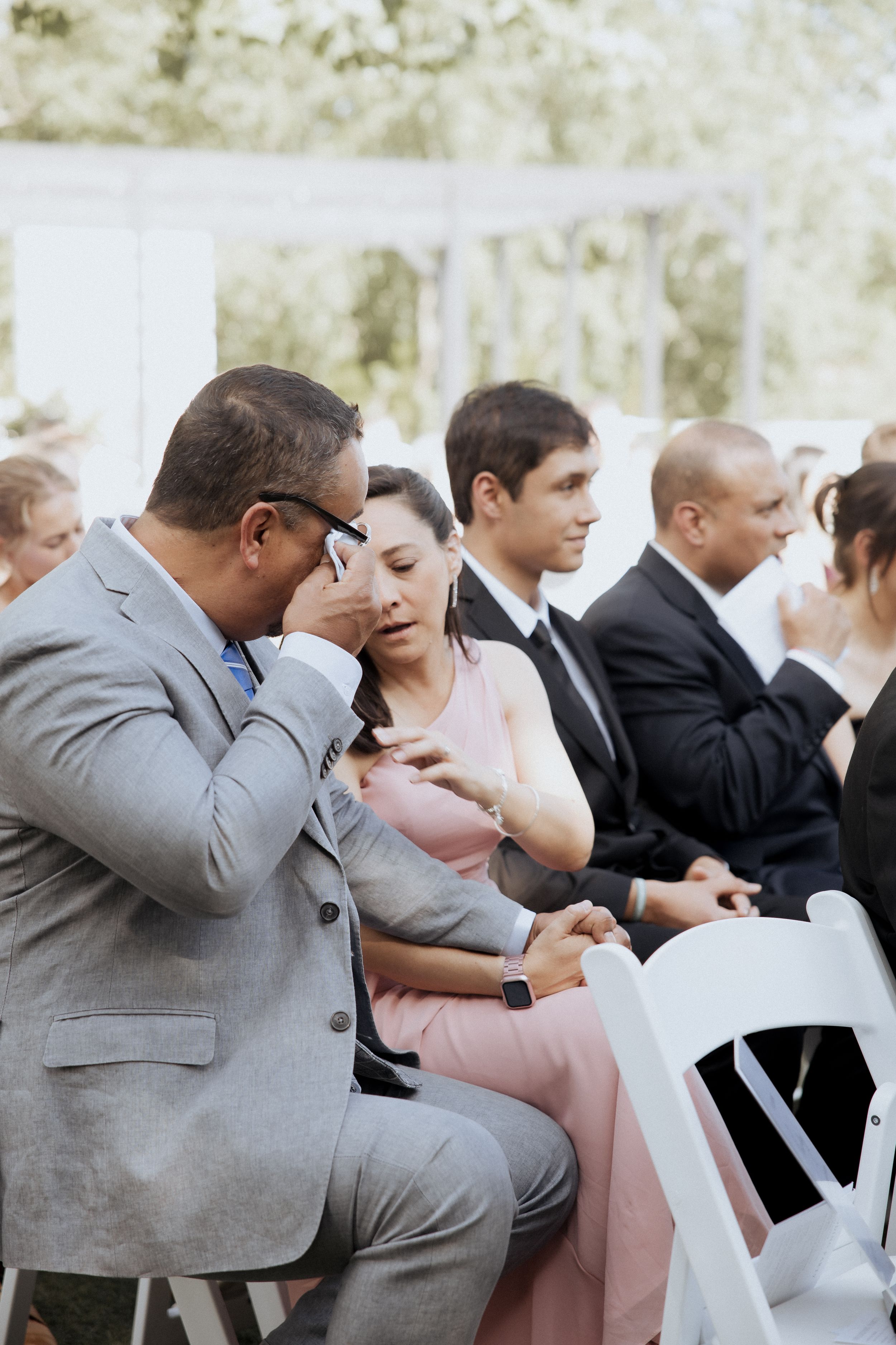 Wedding guests react emotionally during an outdoor ceremony showing various expressions of joy and tears.
