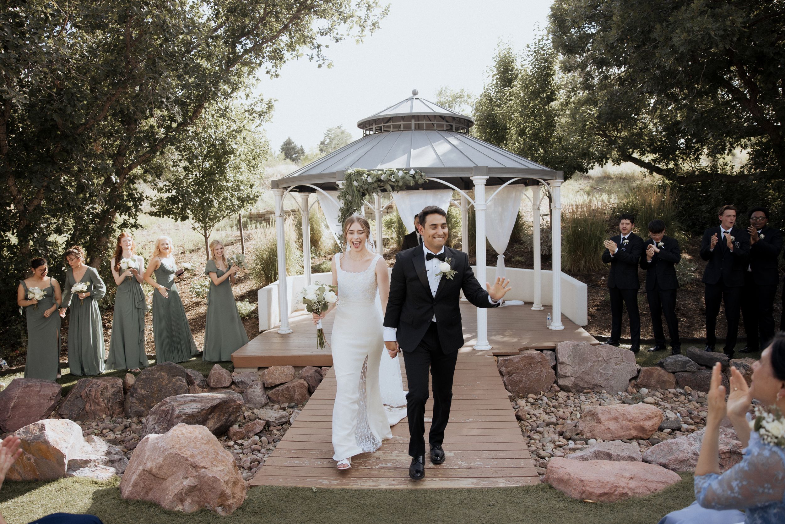 A romantic outdoor wedding ceremony under a gazebo with guests seated on both sides of a stone pathway.