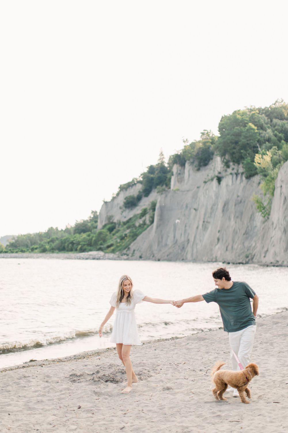 Couple walking on beach with cliffs in background and golden retriever dog.