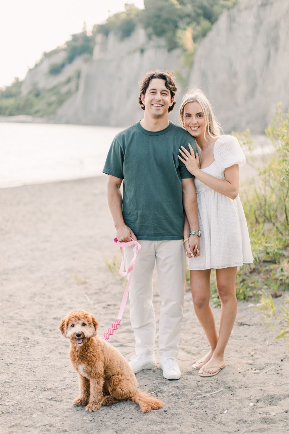 Couple with their goldendoodle puppy enjoying time at a beach with cliffs.