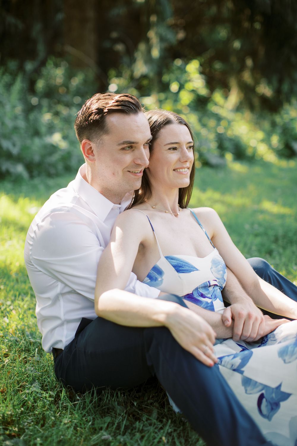Couple lounging on grass in casual attire during a sunny outdoor photo session.