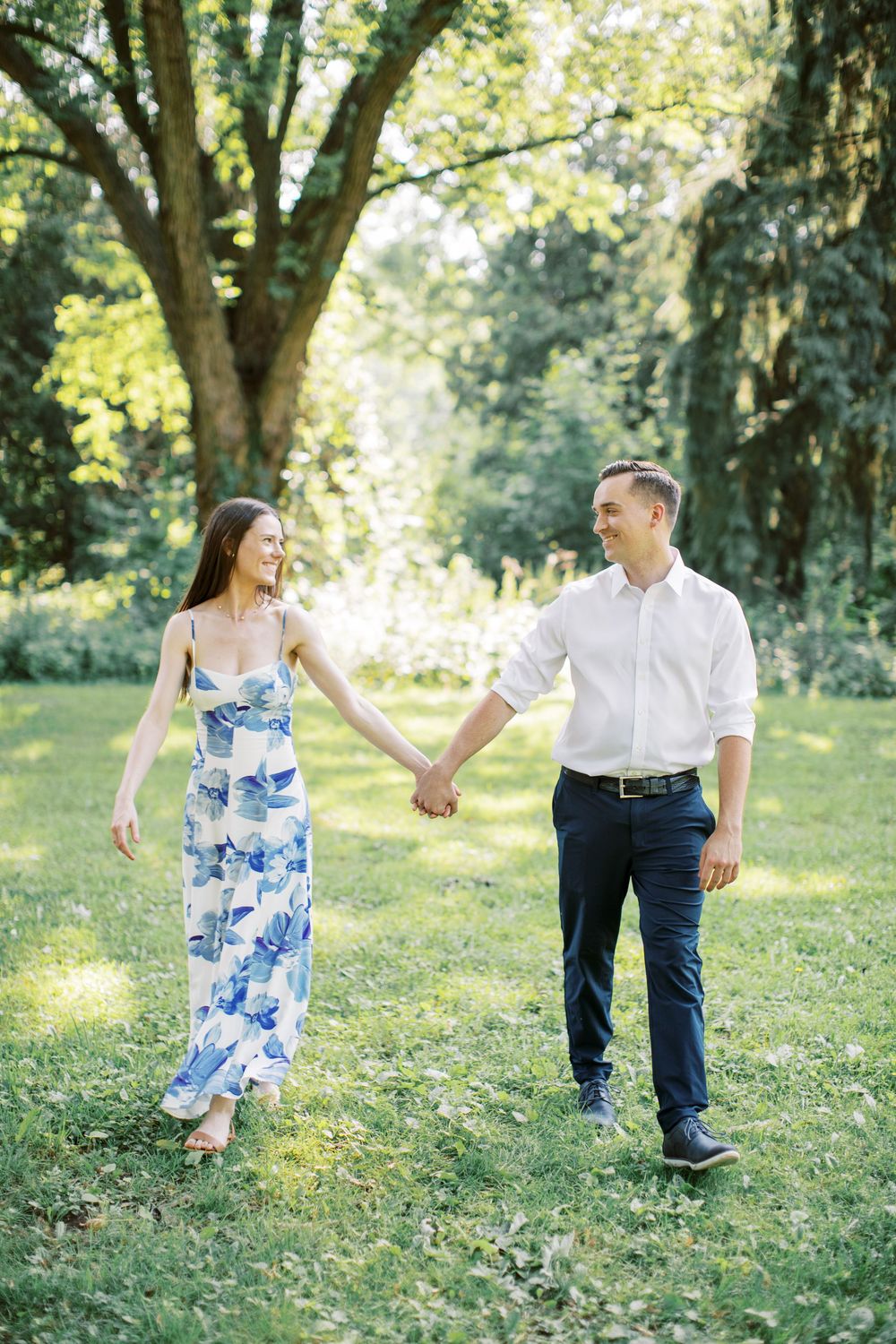 Couple walking hand in hand through sunlit park in summer attire.
