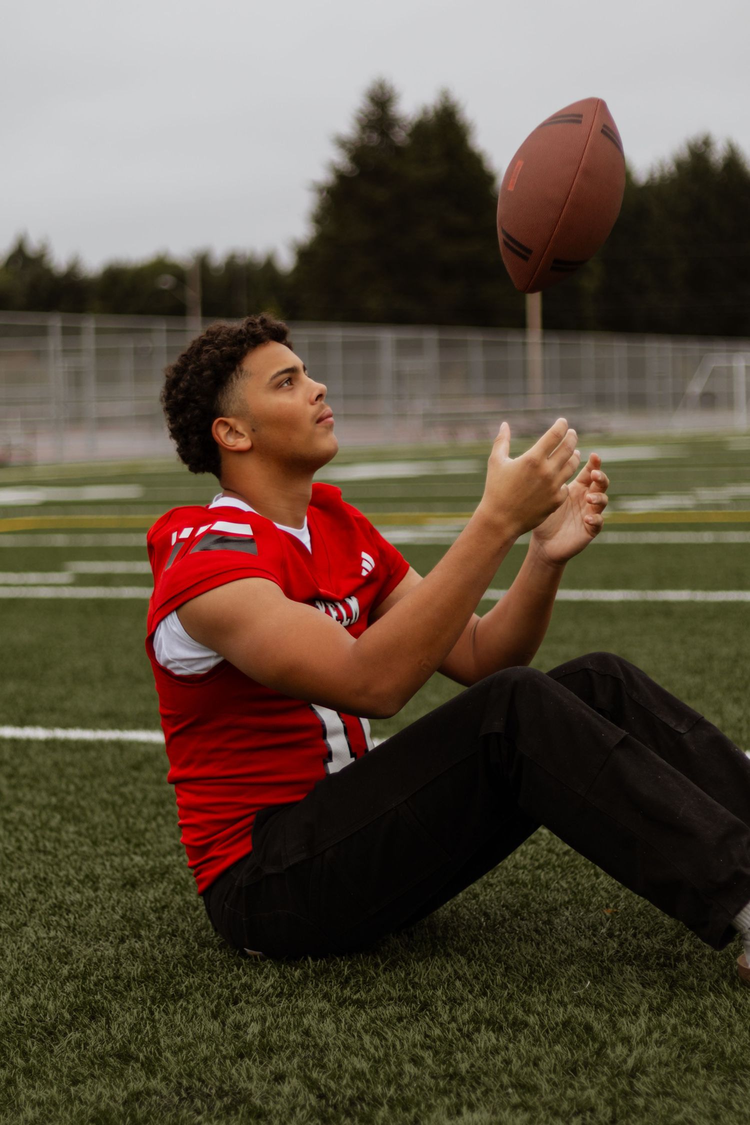 Young male athlete in red jersey tossing a football on a sports field.