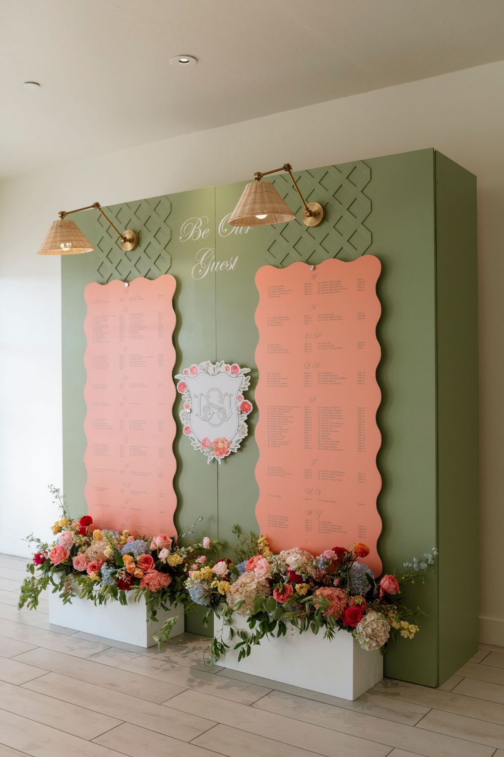 Wedding seating chart display with pink and sage green panels decorated with fresh flowers.