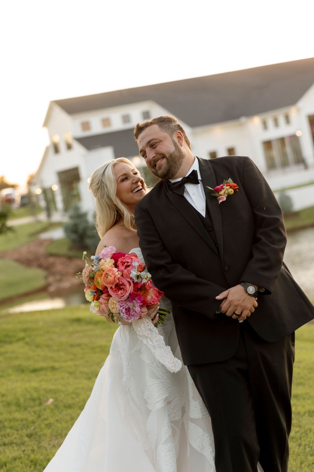 Joyful wedding couple shares candid moments outdoors with vibrant coral bouquet at sunset.