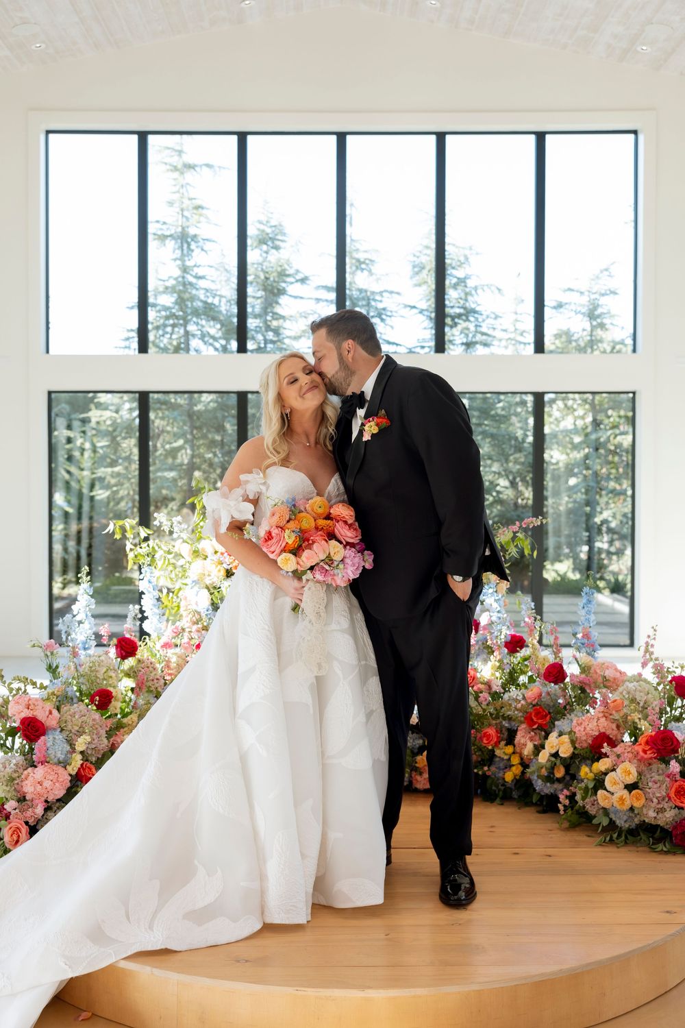 Modern wedding venue with wooden stage and vibrant coral and pink floral arrangements.