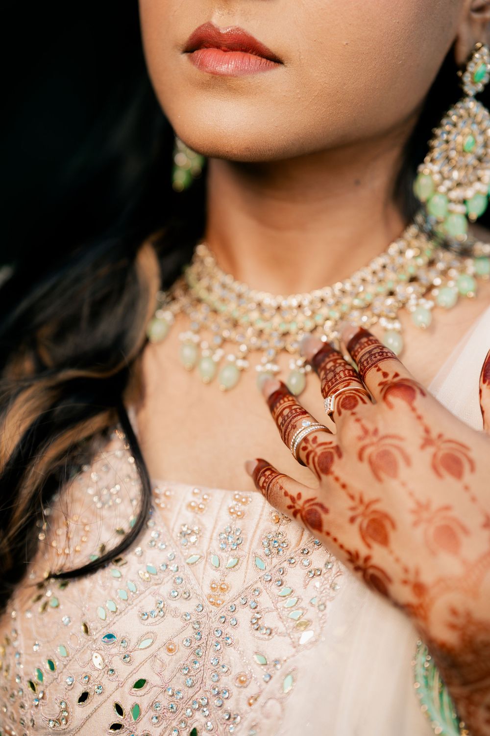 Close-up details of intricate bridal jewelry and henna designs on hands against a light colored traditional outfit.