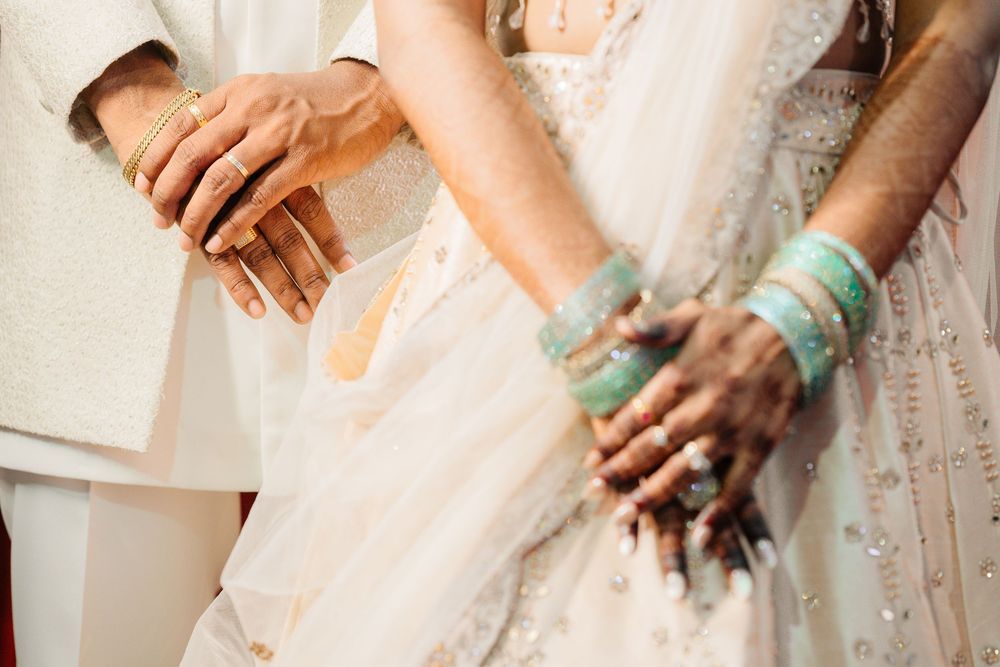 Close-up view of hands wearing turquoise bracelets and rings against white lace and fabric.