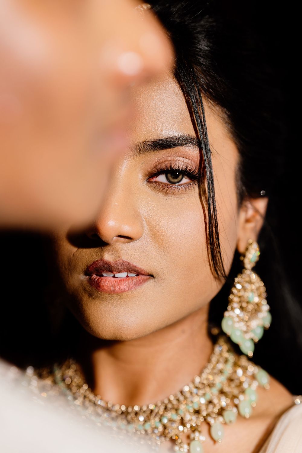 Close-up beauty portrait showing pearl jewelry and traditional Indian bridal accessories against dark background.