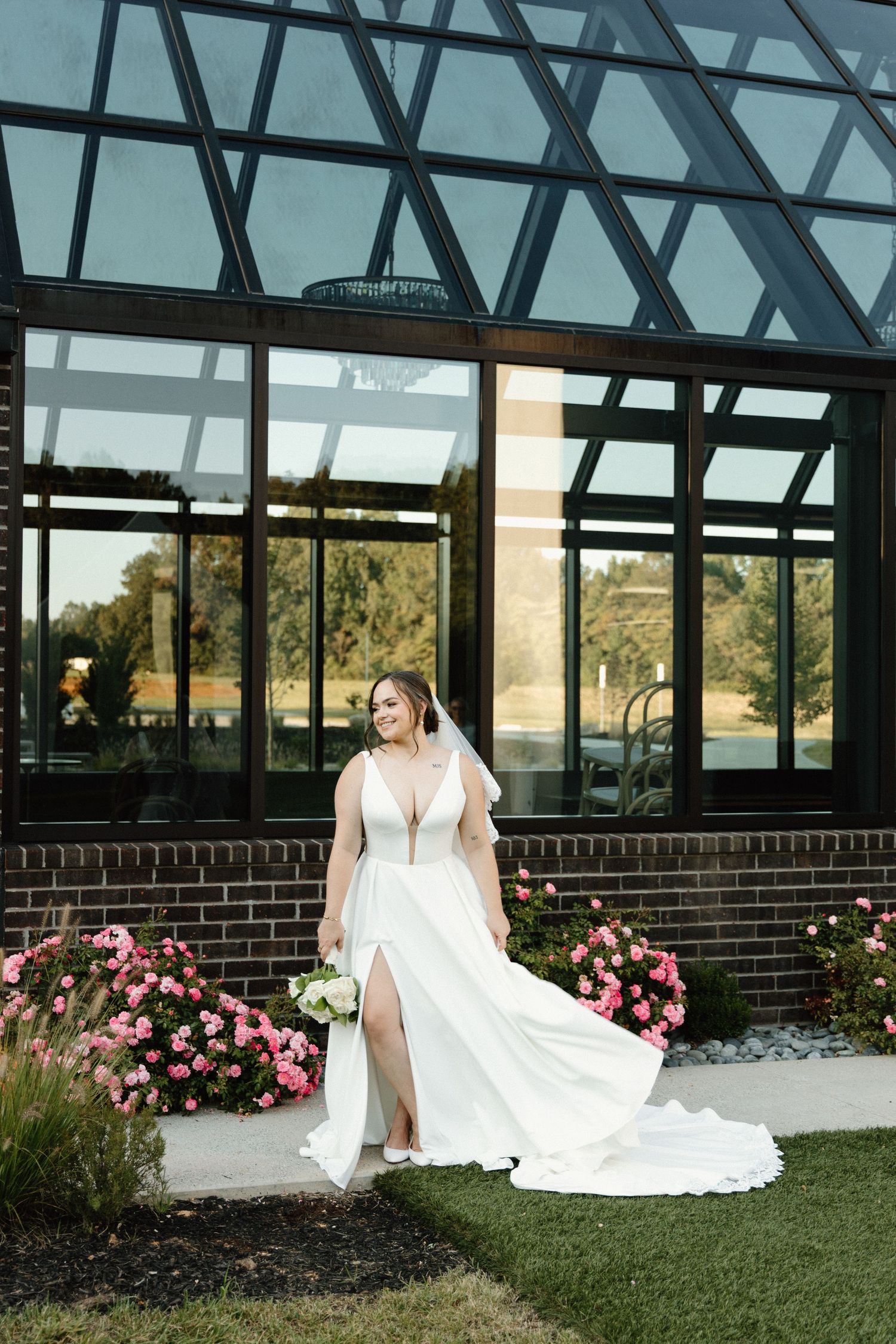 Elegant bridal portraits taken in a glass conservatory with pink flowers blooming outside.