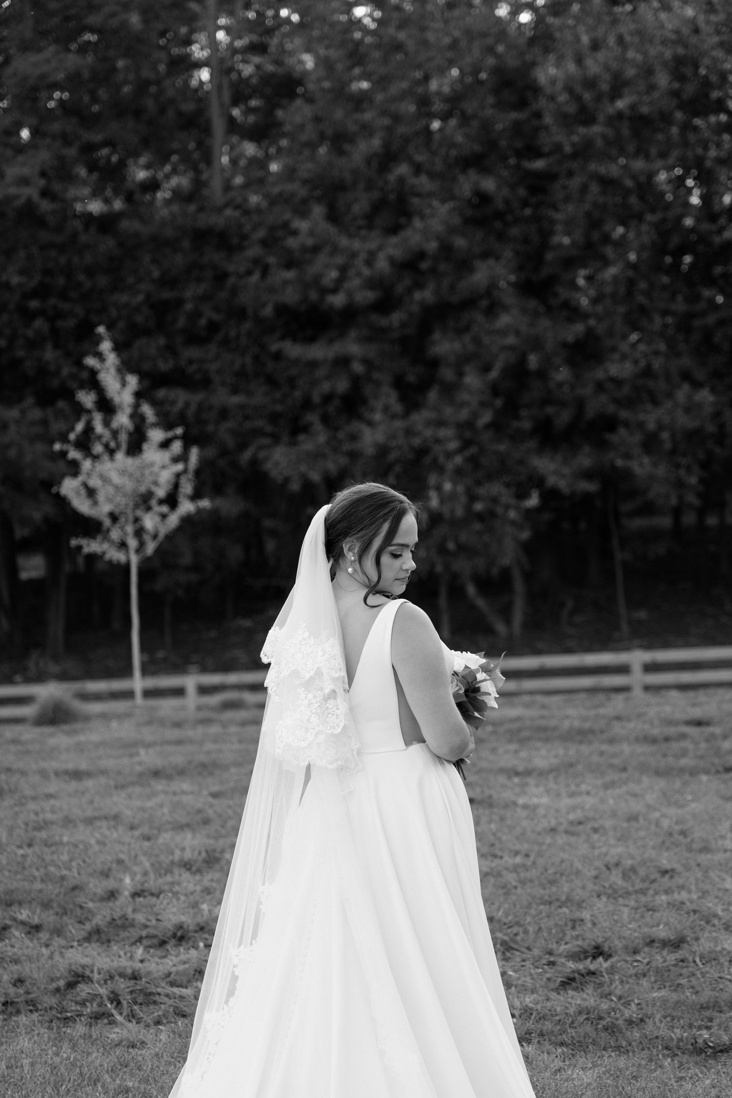 A bride in a flowing white wedding dress and veil walks gracefully across a grassy field on her special day.