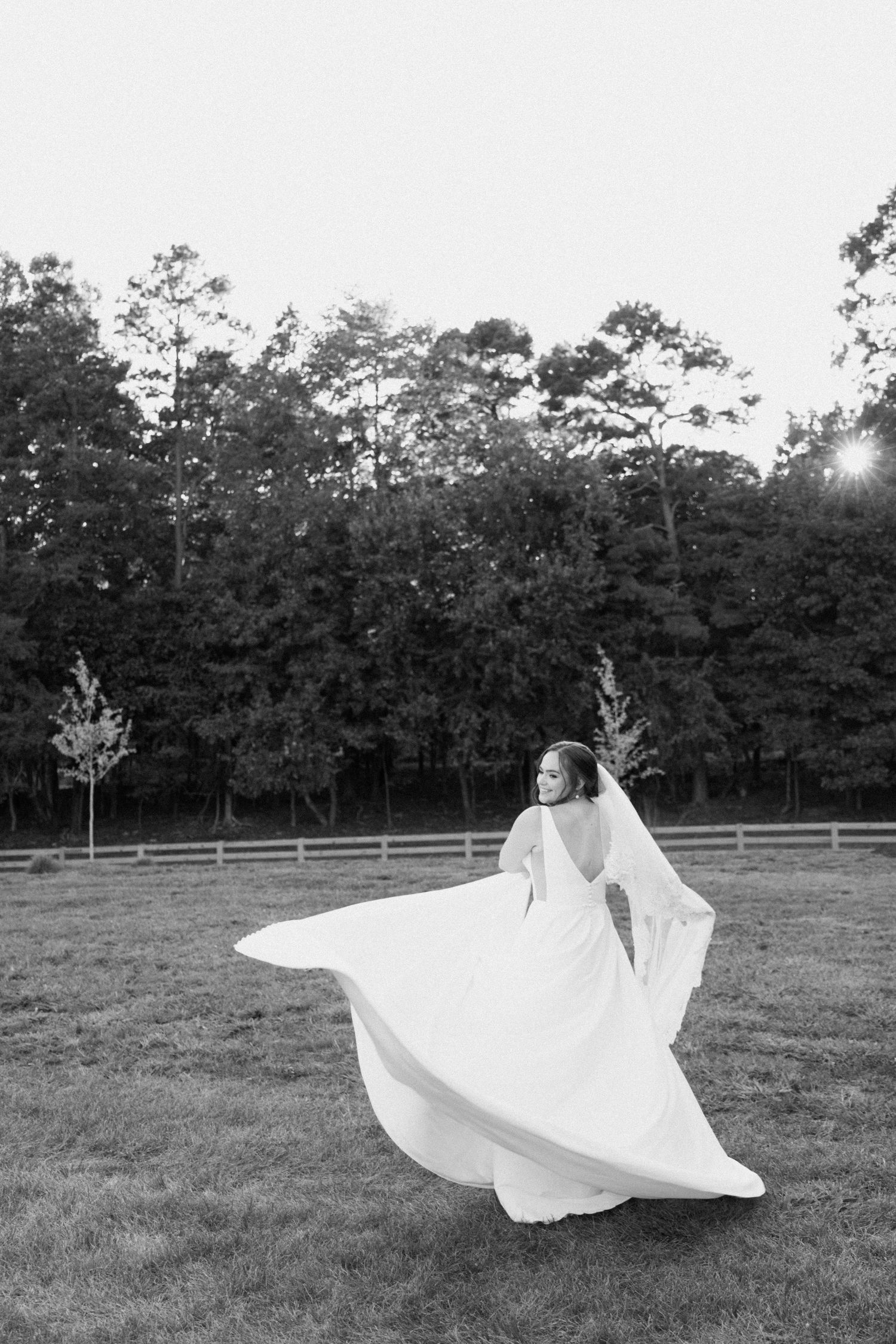 A person in a flowing white dress spins gracefully in a grassy field at sunset with trees in the background.