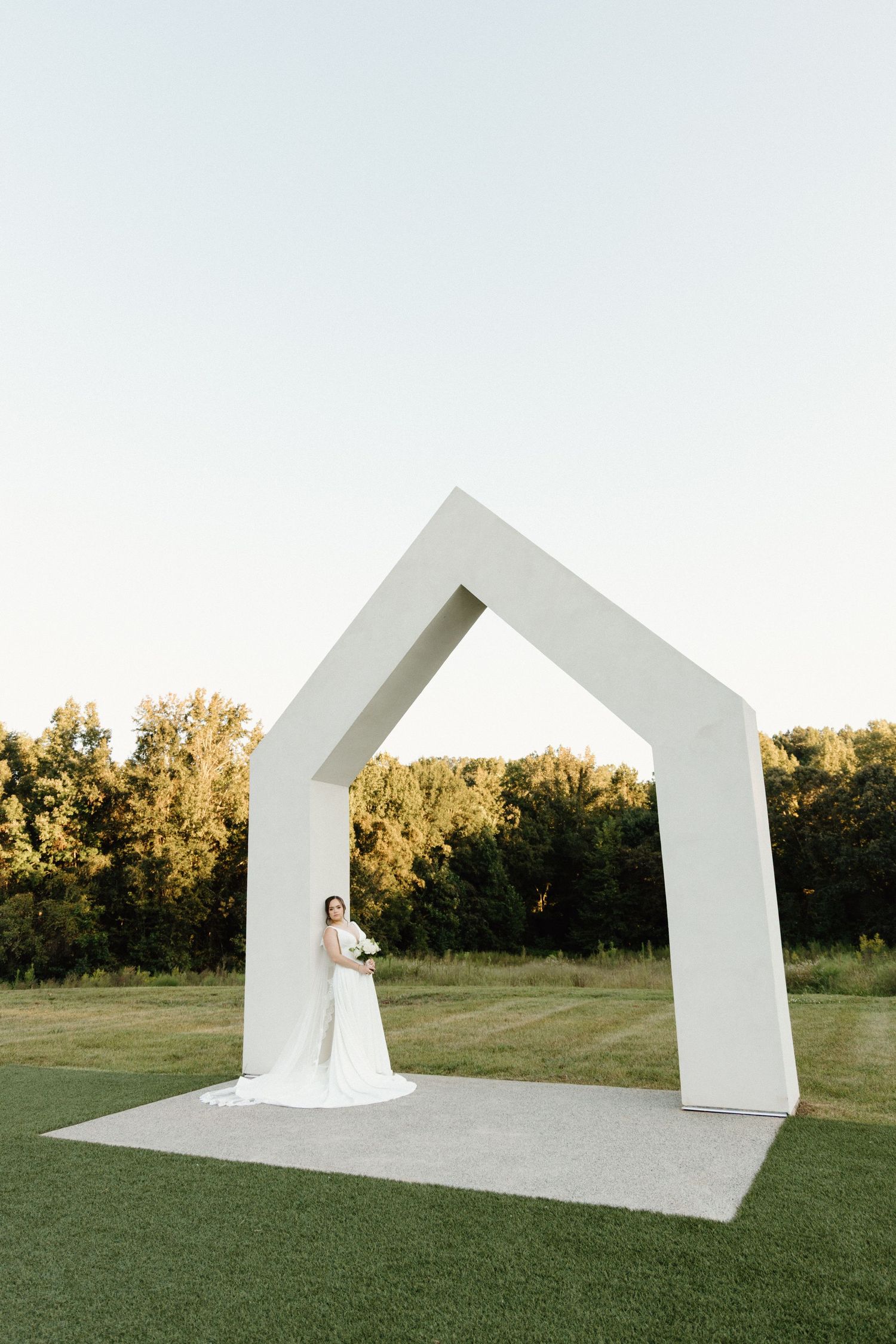 Modern white geometric architectural structures create a striking backdrop in a grassy field at sunset.