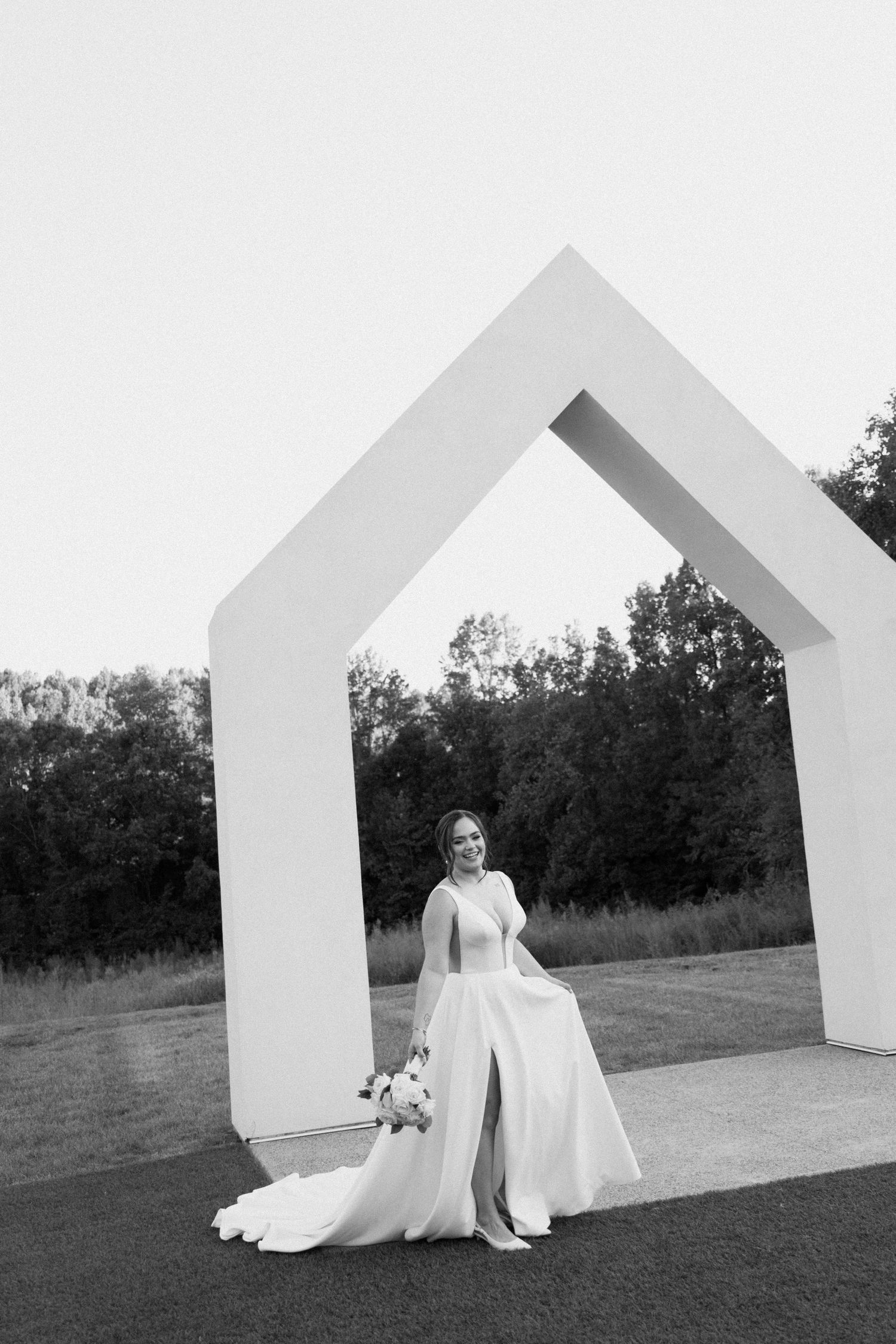 A black and white wedding photo with a couple posing against a series of white geometric house-shaped structures outdoors.