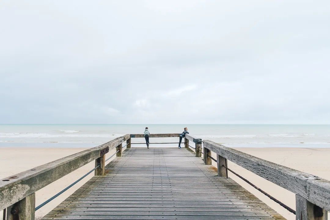 Children standing together on a wooden pier facing the calm ocean.
